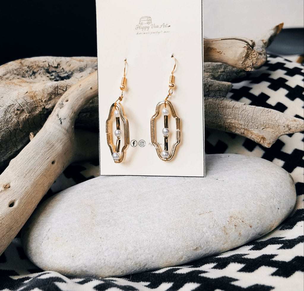Gold earrings on a card with driftwood and stones in the background